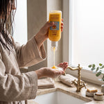 Bienenprodukte Shop API Pflege-Shampoo mit Honig und Gelée Royale, das in die Handfläche einer Frau gegossen wird.