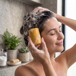 Frau wäscht ihre Haare mit Bienenprodukte Shop festem Honig-Shampoo in einem Badezimmer mit natürlichem Schaum.